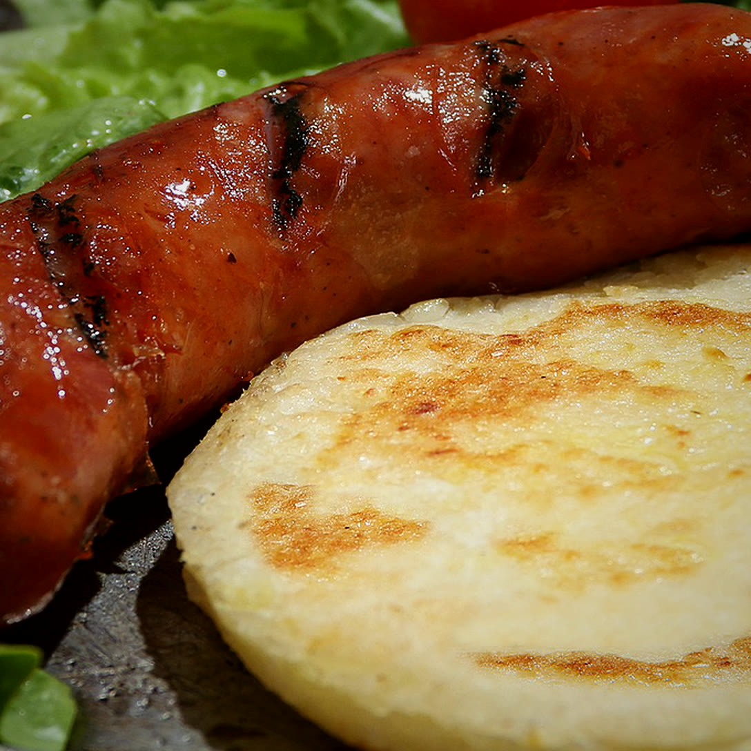 Chorizo asado junto a una arepa.