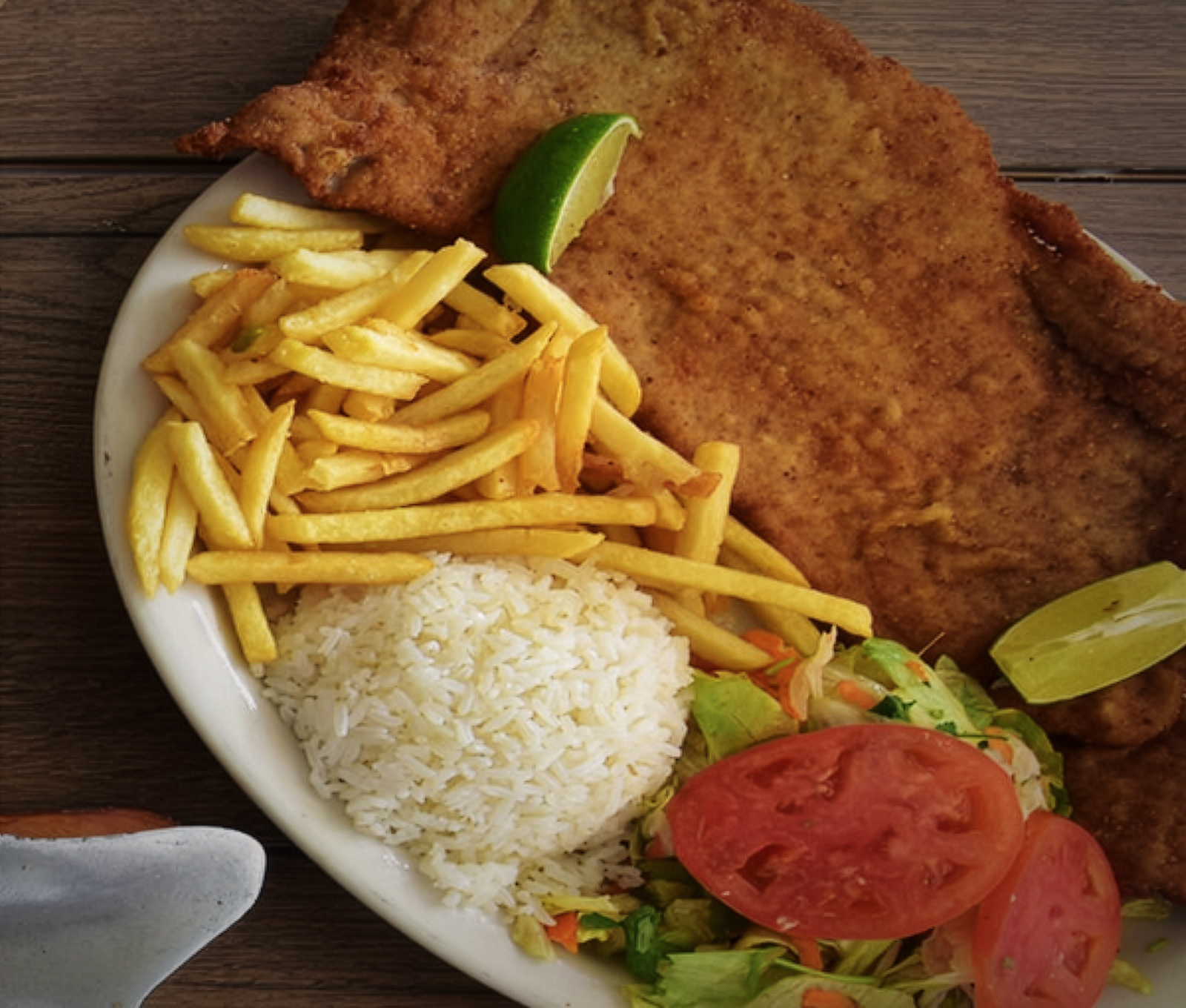 Milanesa apanada con arroz, papas a la francesa, ensalada y limón.